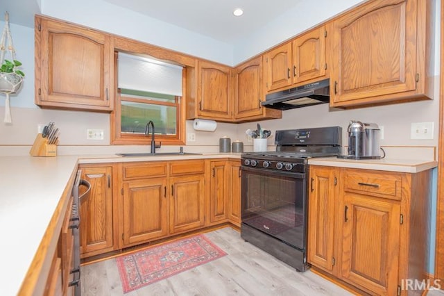 kitchen with a sink, light wood-style floors, gas stove, light countertops, and under cabinet range hood