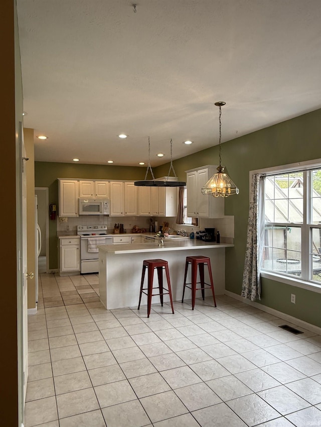 kitchen featuring a peninsula, plenty of natural light, visible vents, and white appliances
