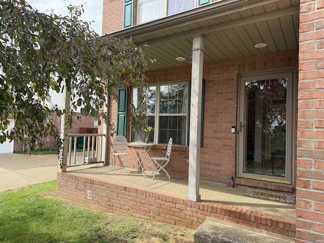 view of exterior entry featuring brick siding and covered porch