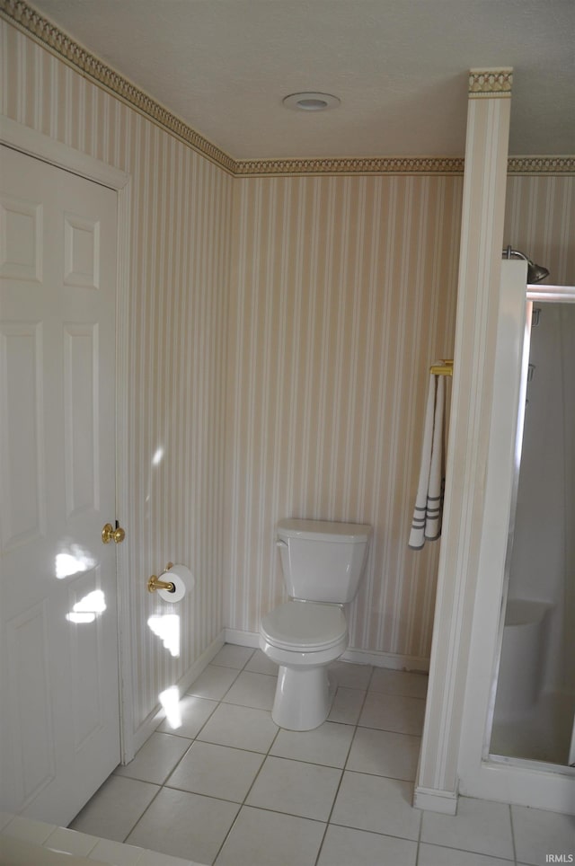 bathroom featuring wallpapered walls, tile patterned floors, toilet, baseboards, and a stall shower