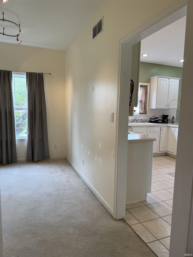 empty room with light carpet, light tile patterned flooring, visible vents, and baseboards