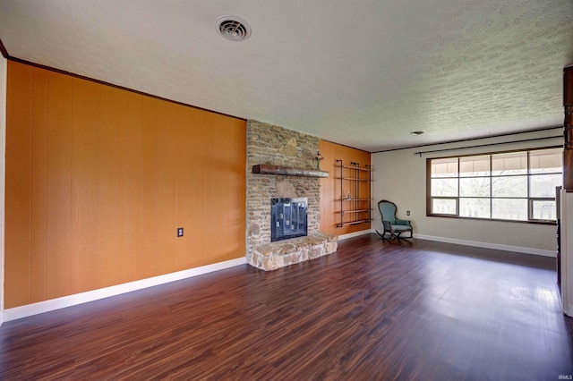 unfurnished living room with a textured ceiling, baseboards, visible vents, a fireplace, and dark wood-type flooring