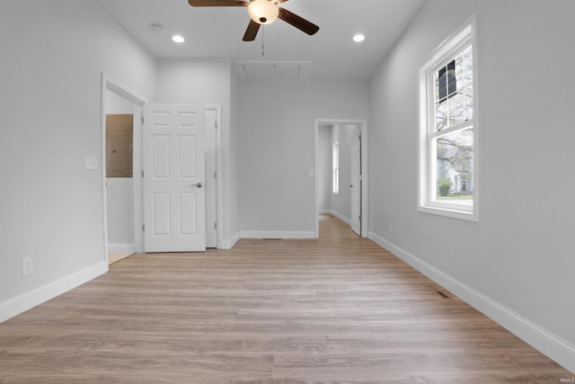 unfurnished bedroom with attic access, light wood-style floors, electric panel, and baseboards