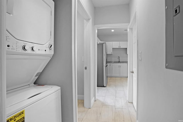 laundry room with marble finish floor, laundry area, a sink, baseboards, and stacked washer and dryer