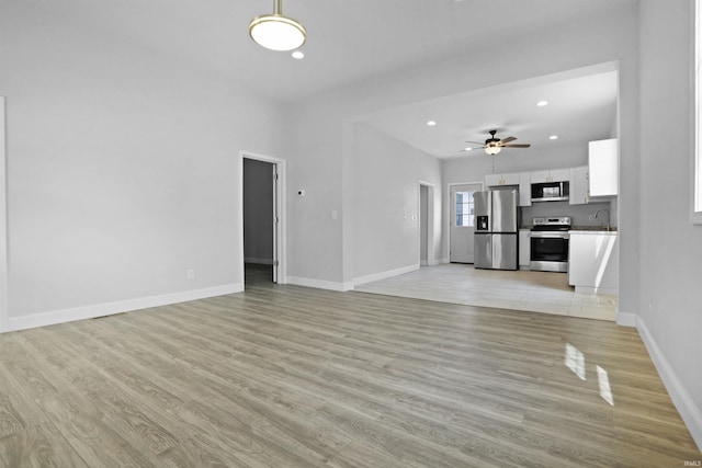unfurnished living room with baseboards, a sink, light wood-type flooring, and recessed lighting