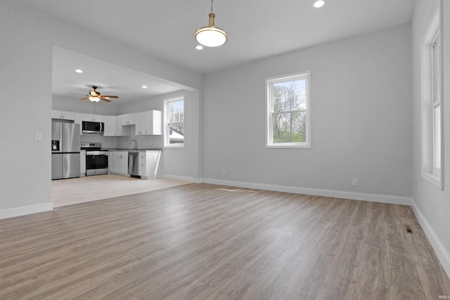 unfurnished living room with recessed lighting, a ceiling fan, a sink, light wood-style floors, and baseboards