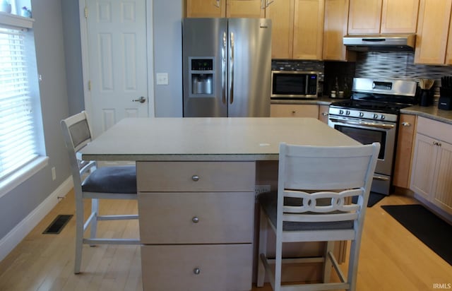 kitchen with under cabinet range hood, baseboards, appliances with stainless steel finishes, and plenty of natural light