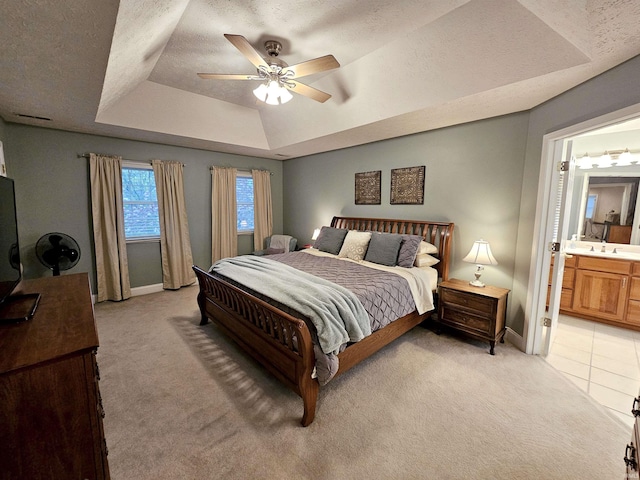 bedroom with a tray ceiling, baseboards, ensuite bath, and light colored carpet