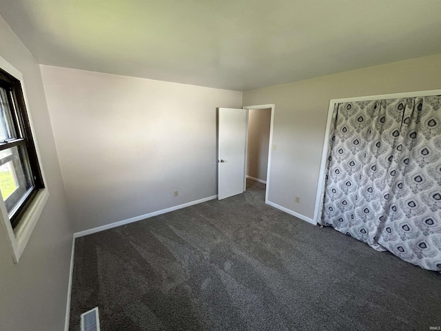 unfurnished bedroom featuring baseboards, dark colored carpet, and visible vents