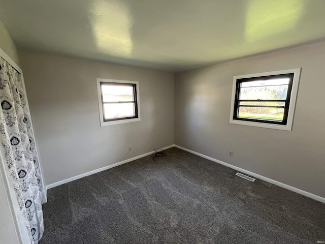 empty room with dark carpet, visible vents, and baseboards
