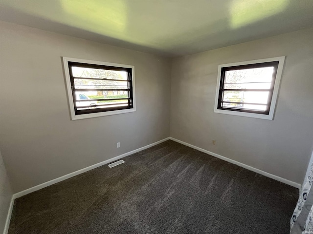 empty room featuring dark carpet, a wealth of natural light, visible vents, and baseboards