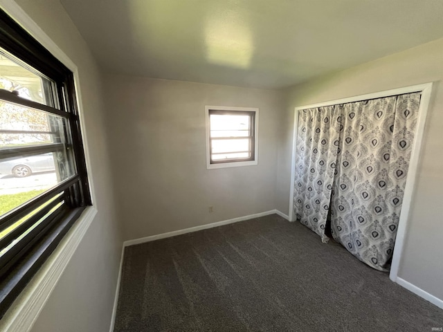 spare room featuring dark carpet and baseboards