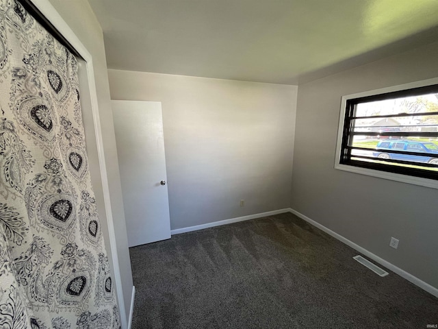 unfurnished room featuring baseboards, dark colored carpet, and visible vents