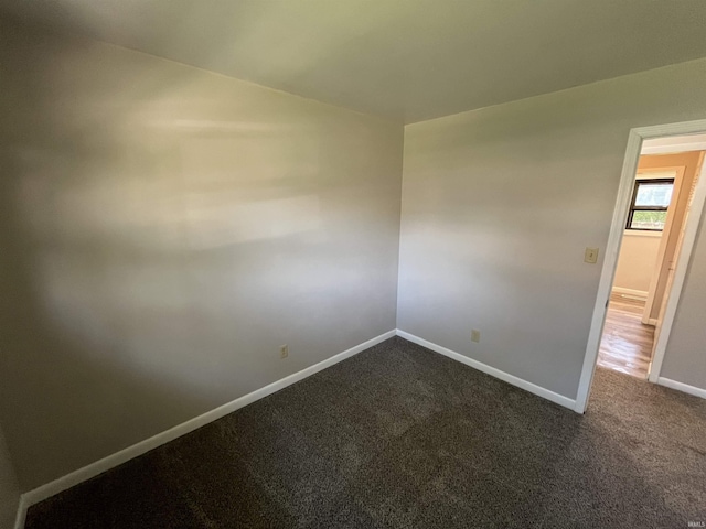 unfurnished room featuring dark colored carpet and baseboards