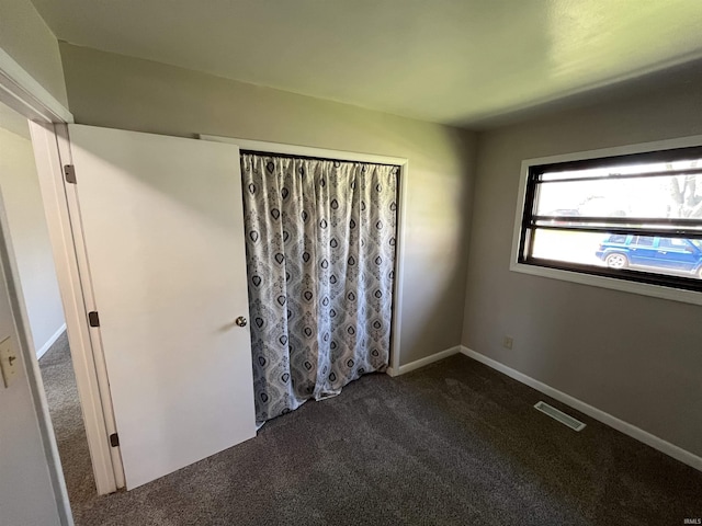 unfurnished room with baseboards, dark colored carpet, and visible vents