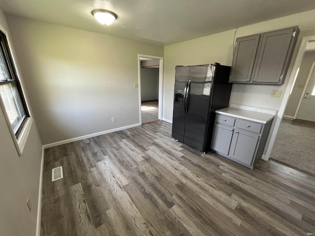 kitchen with wood finished floors, gray cabinetry, light countertops, black fridge, and visible vents