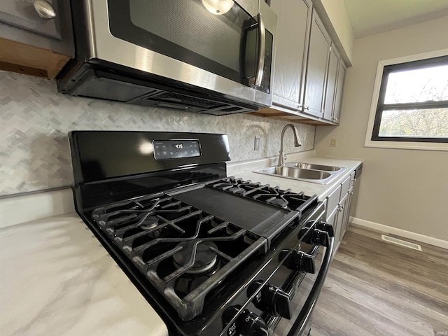 kitchen featuring light countertops, backsplash, a sink, stainless steel microwave, and black gas stove
