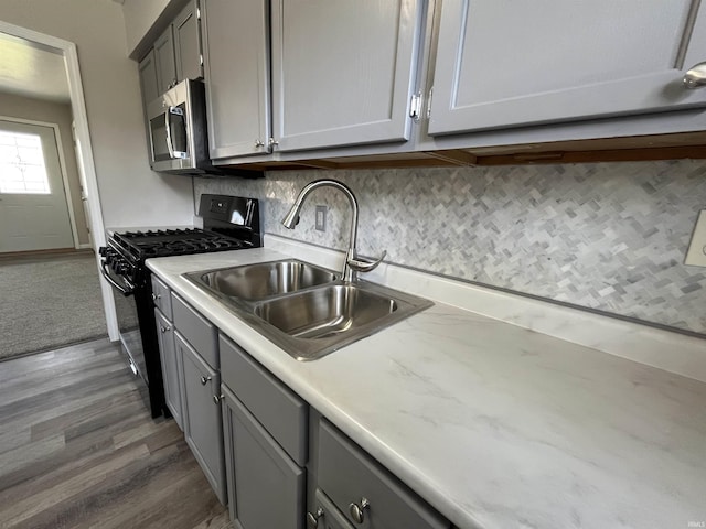 kitchen featuring black gas stove, a sink, stainless steel microwave, and gray cabinets