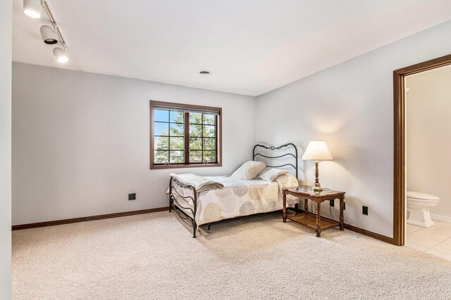 bedroom with baseboards, ensuite bathroom, rail lighting, and light colored carpet