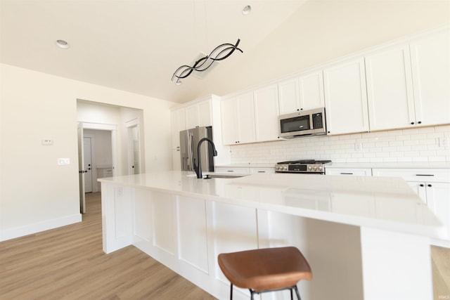 4026 W Carmola Dr, Bloomington, IN 47404 - kitchen featuring a large island with sink, stainless steel appliances, light wood-style flooring, backsplash, and white cabinetry