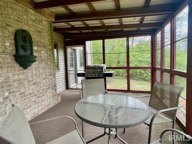 sunroom with brick wall, outdoor dining space, carpet flooring, and beam ceiling