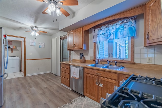 kitchen featuring dishwasher, a ceiling fan, a sink, brown cabinetry, and washer / clothes dryer