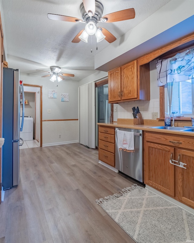 kitchen featuring a sink, a ceiling fan, brown cabinets, appliances with stainless steel finishes, and washer / dryer