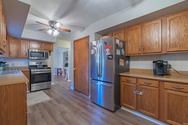 kitchen with a ceiling fan, wood finished floors, a sink, decorative backsplash, and appliances with stainless steel finishes