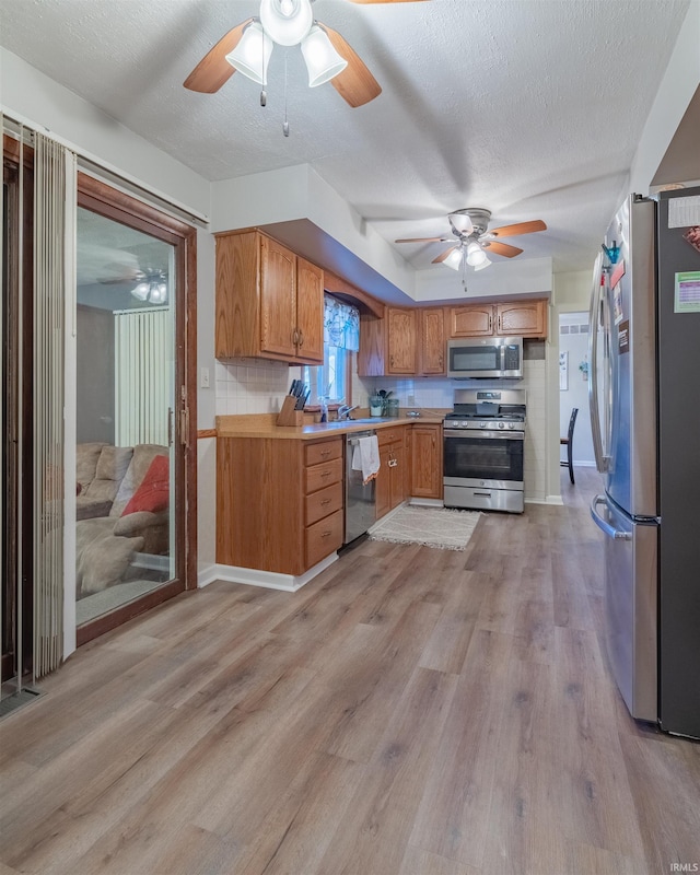 kitchen with ceiling fan, stainless steel appliances, light wood finished floors, and light countertops