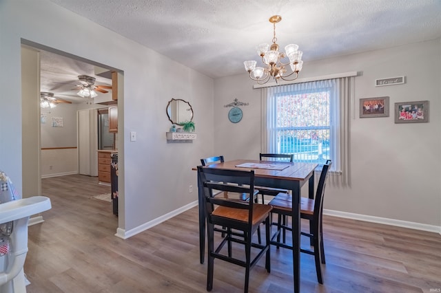 dining room with ceiling fan with notable chandelier, baseboards, wood finished floors, and a textured ceiling
