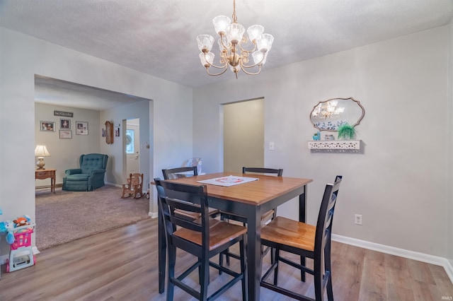 dining space featuring a chandelier, wood finished floors, a textured ceiling, and baseboards