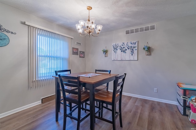 dining space featuring wood finished floors, visible vents, a textured ceiling, and a notable chandelier