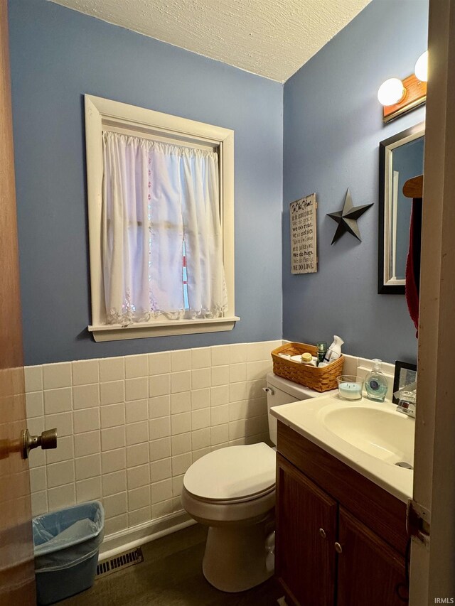 bathroom featuring a textured ceiling, toilet, tile walls, visible vents, and vanity