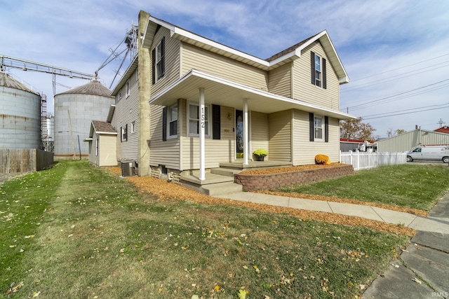 traditional home featuring a porch, a front lawn, fence, and central AC