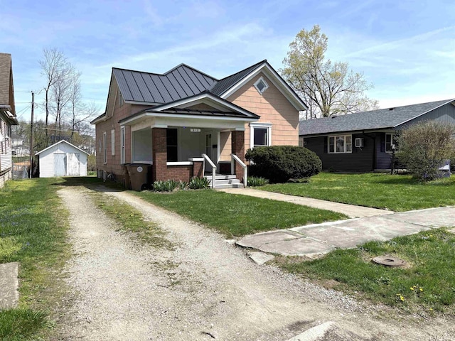 bungalow-style house with a front lawn, a porch, brick siding, an outdoor structure, and dirt driveway
