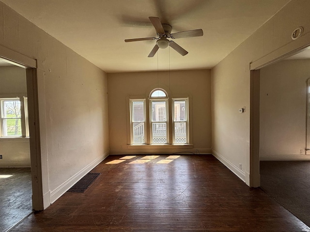 empty room featuring baseboards, a ceiling fan, dark wood-type flooring, and visible vents