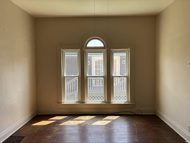 spare room featuring visible vents, baseboards, and dark wood-style flooring
