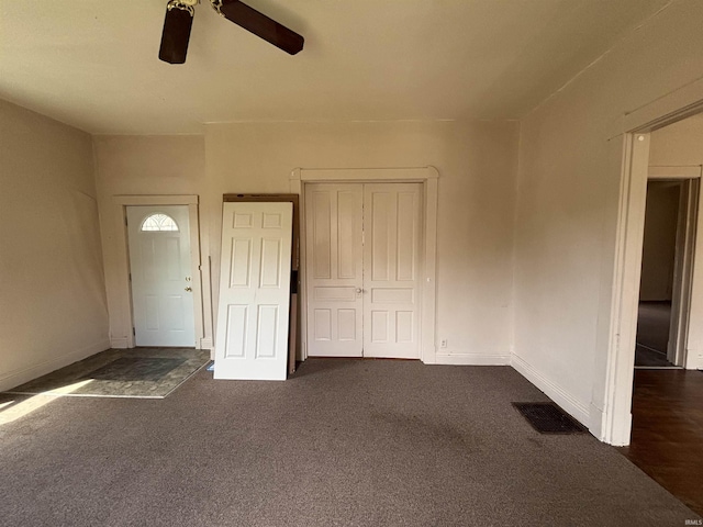 foyer entrance featuring visible vents, a ceiling fan, baseboards, and dark carpet