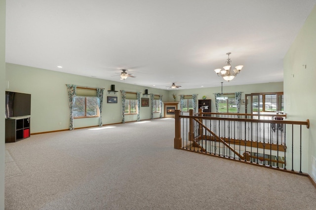 empty room featuring ceiling fan with notable chandelier, baseboards, carpet flooring, and a warm lit fireplace