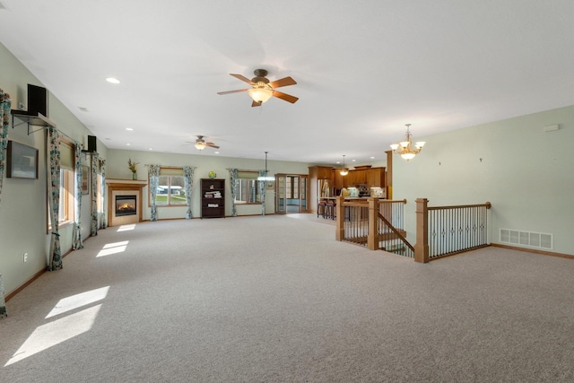 unfurnished living room with ceiling fan with notable chandelier, light carpet, baseboards, visible vents, and recessed lighting