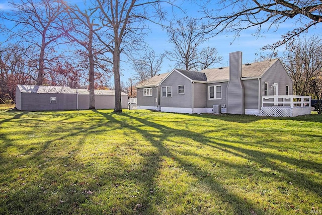 rear view of property featuring a chimney, a deck, central AC, and a lawn