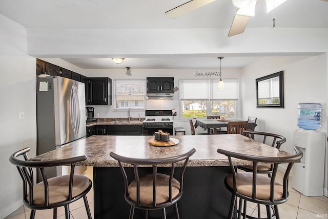 kitchen featuring a breakfast bar area, a sink, gas range, under cabinet range hood, and light tile patterned floors