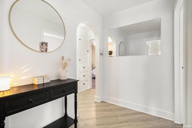 hallway featuring arched walkways, baseboards, and light wood-style floors