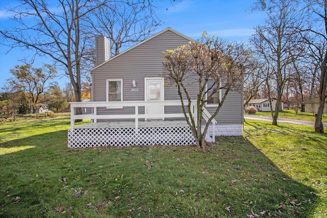 rear view of property featuring a lawn, a chimney, and a deck