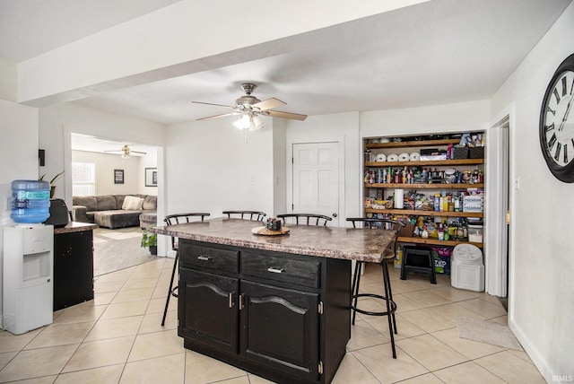 kitchen featuring dark cabinets, a kitchen breakfast bar, ceiling fan, and light tile patterned flooring