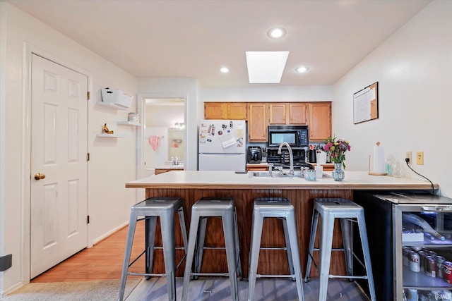 kitchen featuring freestanding refrigerator, black microwave, a breakfast bar, and light wood-type flooring
