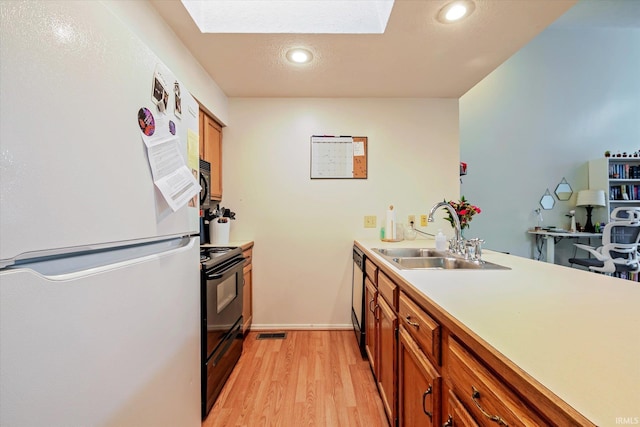 kitchen with brown cabinets, a sink, light wood finished floors, a skylight, and black appliances