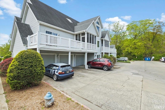 exterior space with a sunroom, an attached garage, driveway, and roof with shingles