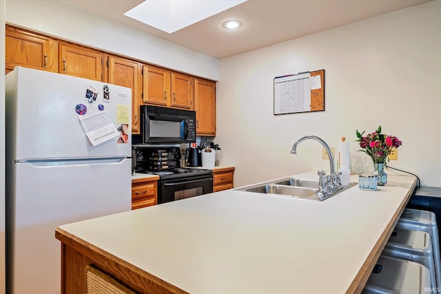 kitchen featuring brown cabinetry, a peninsula, a sink, black appliances, and a skylight