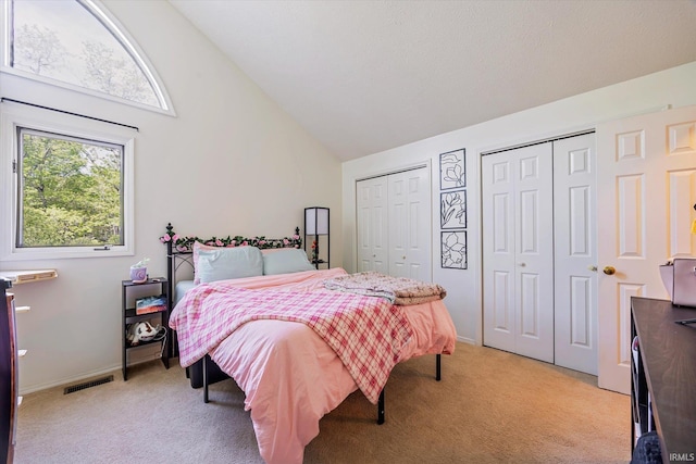 bedroom featuring high vaulted ceiling, multiple closets, light carpet, and visible vents